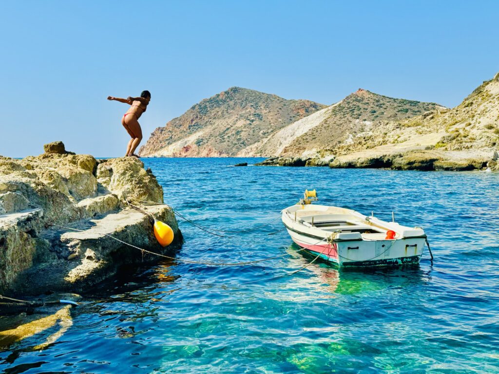 Person preparing to dive into a vivid blue cove with boat nearby